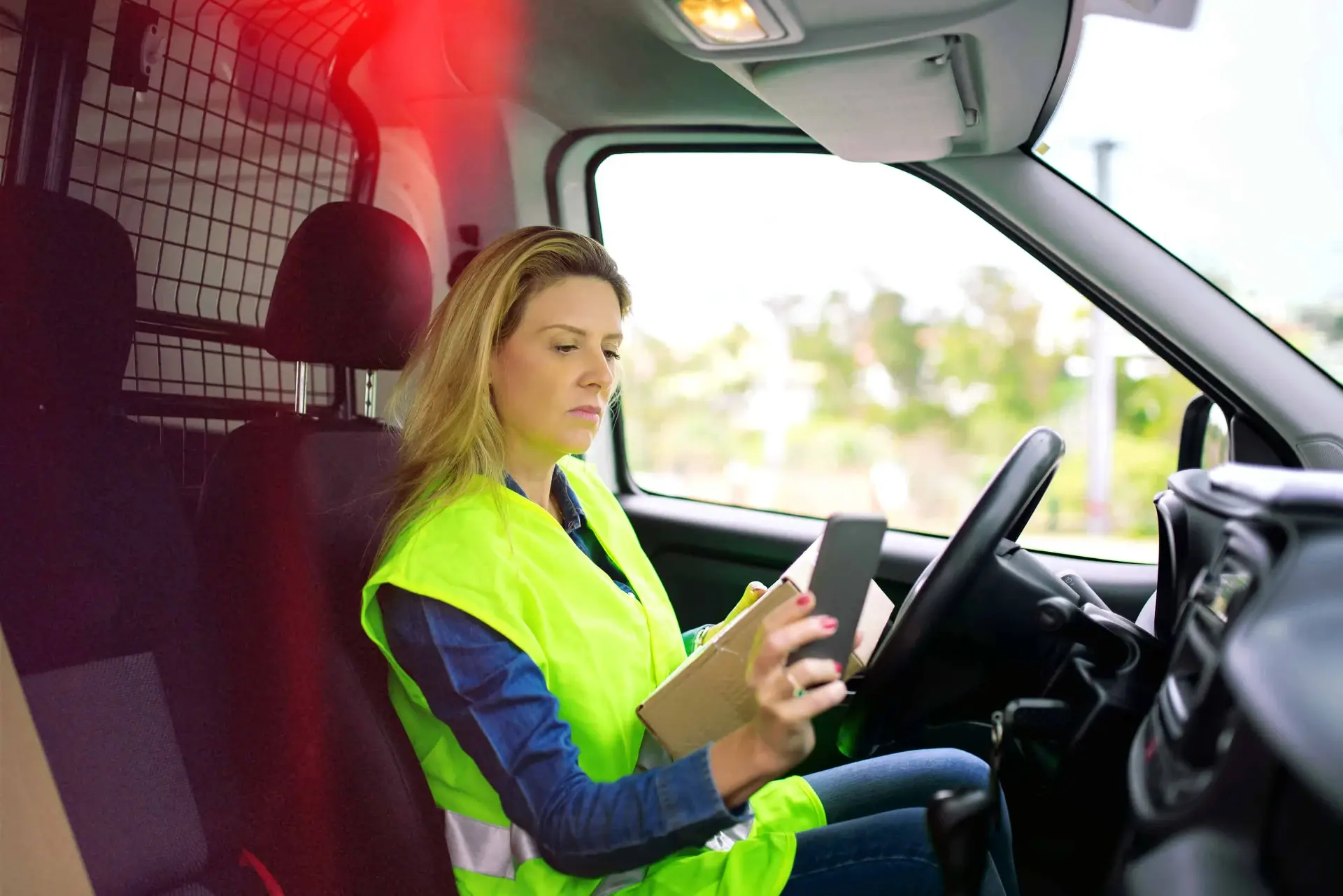 Van driver in high-visibility vest checking tablet while in vehicle